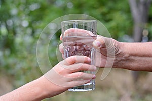 Child giving glass of water to elderly woman outdoors, closeup