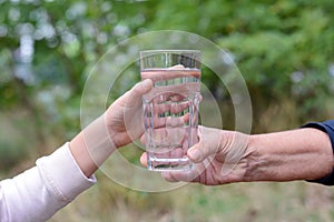 Child giving glass of water to elderly woman outdoors, closeup