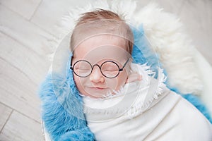 Child with glasses, newborn baby boy in a cocoon in a white bowl on a blue rug