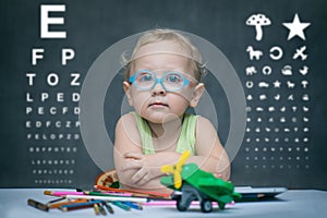 Child with glasses sits at a table on the background of the table for an eye examination