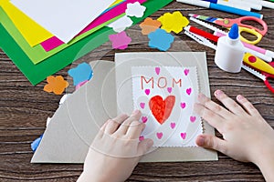The child glues the details from the paper to the postcard. Greeting card with flowers on Mother`s Day.