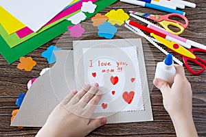 The child glues the details from the paper to the postcard. Greeting card with flowers on Mother`s Day.