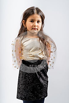 A child in a gold blouse with transparent sleeves, black, corduroy skirt and blue tights isolated on a white background.