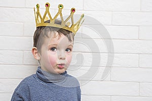 Child with a golden crown on his head against a brick wall background