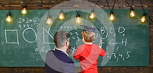 Child in graduate cap listening teacher, chalkboard on background, rear view. Instructive conversation concept. Teacher photo