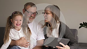 Child and grandparents using pc tablet. Loving middle age couple and their little granddaughter using a digital tablet