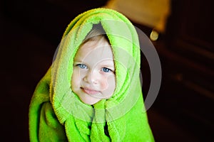 Child with green fleece blanket on his head on a dark background