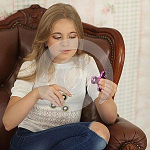 Child with green and pink fidget spinners in hands, sitting in leather chair.
