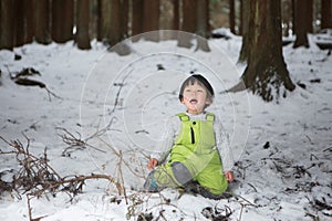 Child in green thermal clothing playing in the snow in the forest