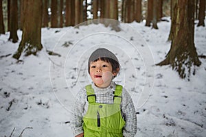 Child in green thermal clothing playing in the snow in the forest