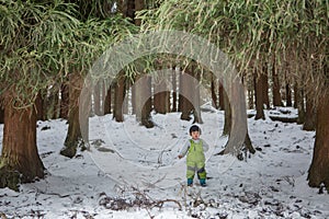 Child in green thermal clothing playing in the snow in the forest