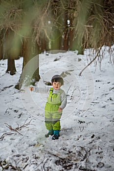 Child in green thermal clothing playing in the snow in the forest