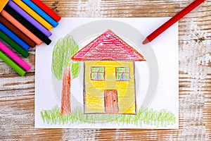 Child hand drawing House with wax crayons. Wood background