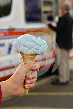 Child hand holding blue buble gum ice cream cone, outdoor. Summer food