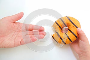 Child hand holds a bitten orange  donut holds out his mom hands on a white background
