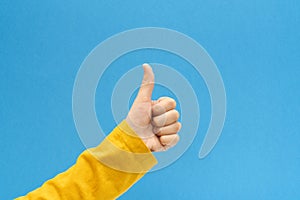 Child hand making thumb up gesture on bright blue background