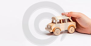 Child hand playing with natural wooden car toy on white backgrou