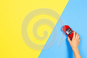 Child hand playing red toy car on light blue and yellow background