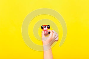 Child hand playing with wooden toy car on yellow background