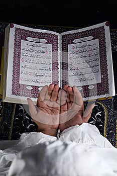 child hand praying with raised hands against the Quran background. Islamic concept