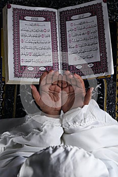 child hand praying with raised hands against the Quran background. Islamic concept