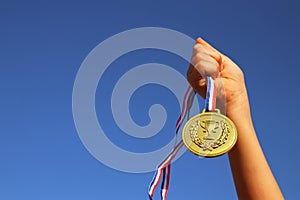 Child hand raised, holding gold medal against sky. education, success, achievement, award and victory concept.