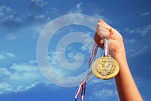 Child hand raised, holding gold medal against sky. education, success, achievement, award and victory concept.