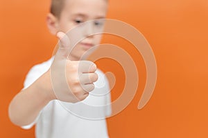 Child hand shows thump up. Focus on the hand. Little boy blurred in the background. Positive sign of agreement and like