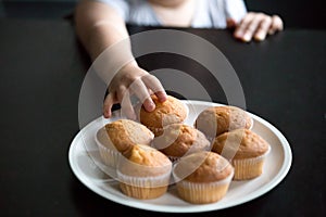 Child hand taking muffins on table close up