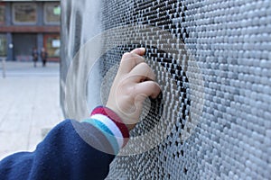 A child hand touching a mosaic of white black and grey tesserae in a street.