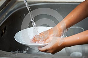 Child hand washing dishes over the sink photo