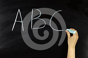 child hand writes on the blackboard abc