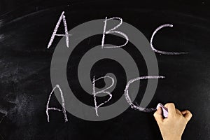 child hand writes on the blackboard abc