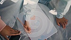 Child hands coloring picture sitting on blanket outdoors with mother close up.