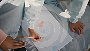 Child hands coloring picture sitting on blanket outdoors with mother close up.