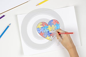 Child hands coloring puzzle heart with colored pencils. Top view. World autism awareness day concept