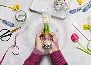 Child hands hold hand painted glass vase with different motifs and white hyacinthine flower in it.