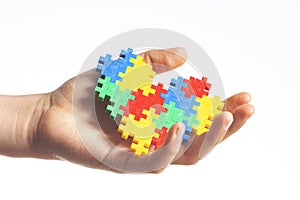 Child hands holding colorful puzzle heart on white background. World autism awareness day concept