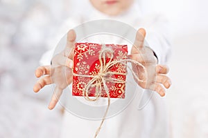 Child hands holding  gift box wrapped in kraft red paper tied on light background. Holiday concept. Christmas holidays. Black