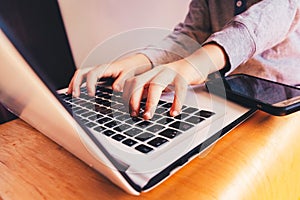 Child hands on laptop computer keyboard next to a mobile phone to do business