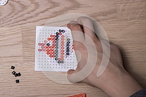 Child hands make beads art in the shape of a fish