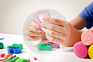 Child hands playing with modeling clay or plasticine on white table