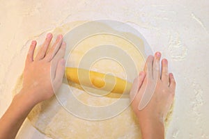 Child hands rolls dough for baking on table on photo