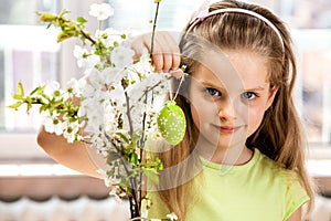 Child hang easter egg on cherry branch.