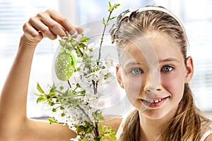 Child hang easter egg on cherry branch.