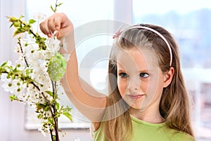 Child hang easter egg on cherry branch