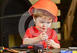 Child in hard hat, helmet playing with hex bolts as builder or repairer, handcrafting. Toddler on busy face plays with