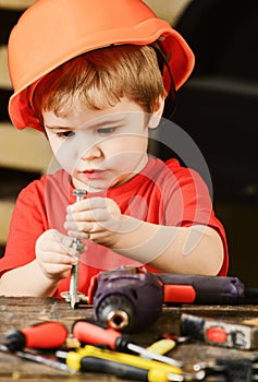 Child in hard hat, helmet playing with hex bolts as builder or repairer, handcrafting. Toddler on busy face plays with