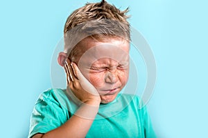 Child has earache. School boy has sore ear. Little kid covered ear with hand and closed eyes. Kid suffering from otitis photo