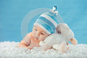 Child in hat hugging toy on a white bedspread photo